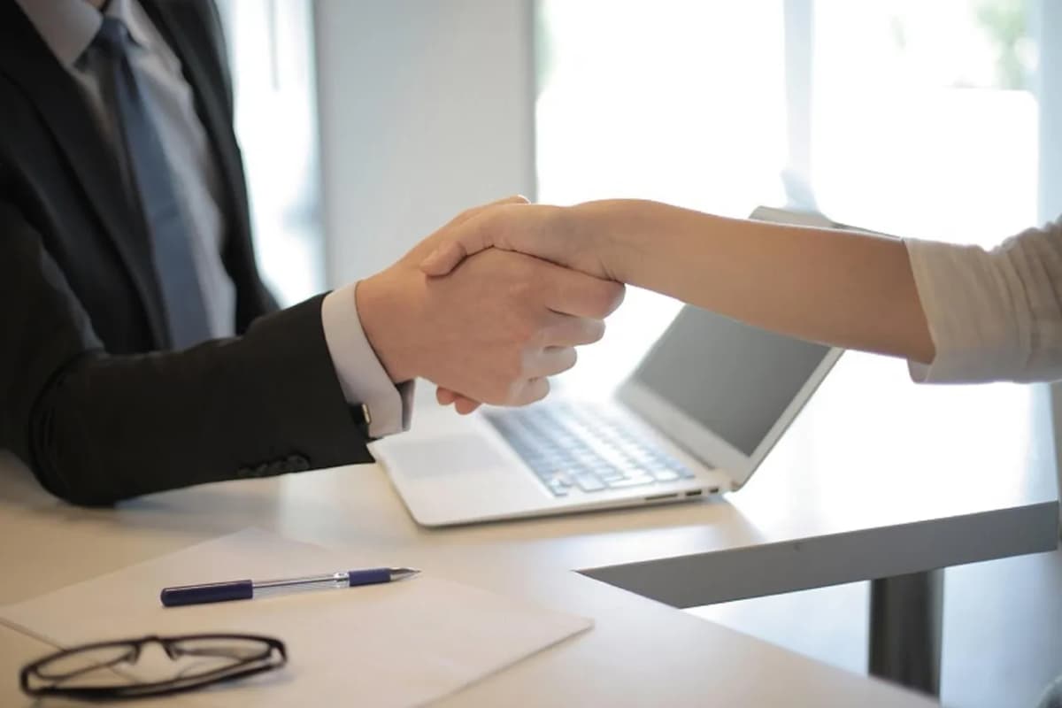 Two people shaking hands across a table at a job interview