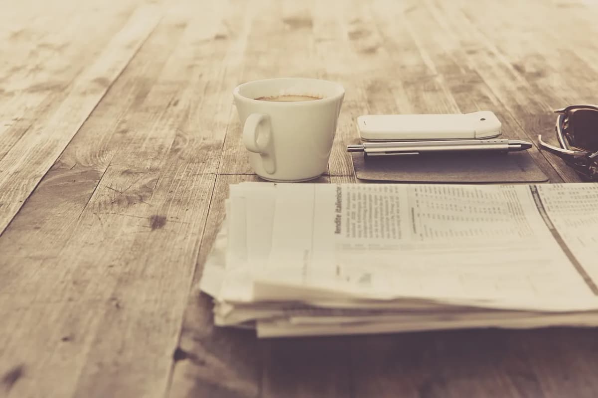 Folded newspapers beside a cup of coffee on a wooden table