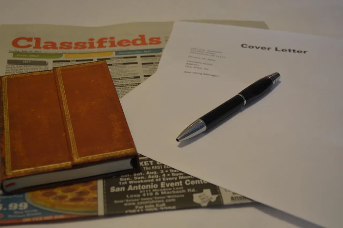 Cover letter and pen on top of newspaper classified job ads and a notebook