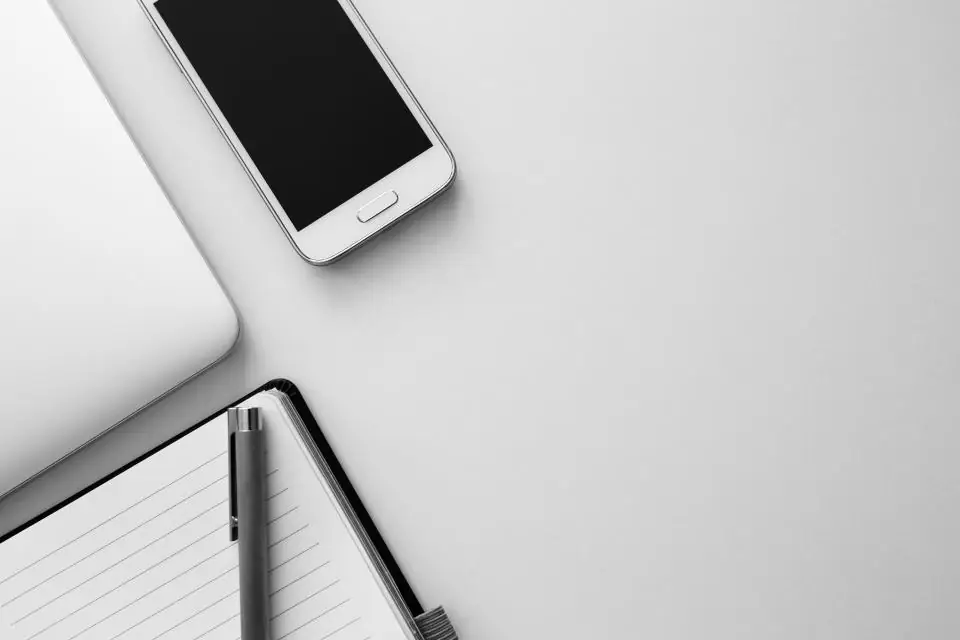A smartphone and a notebook with a pen on a white desk