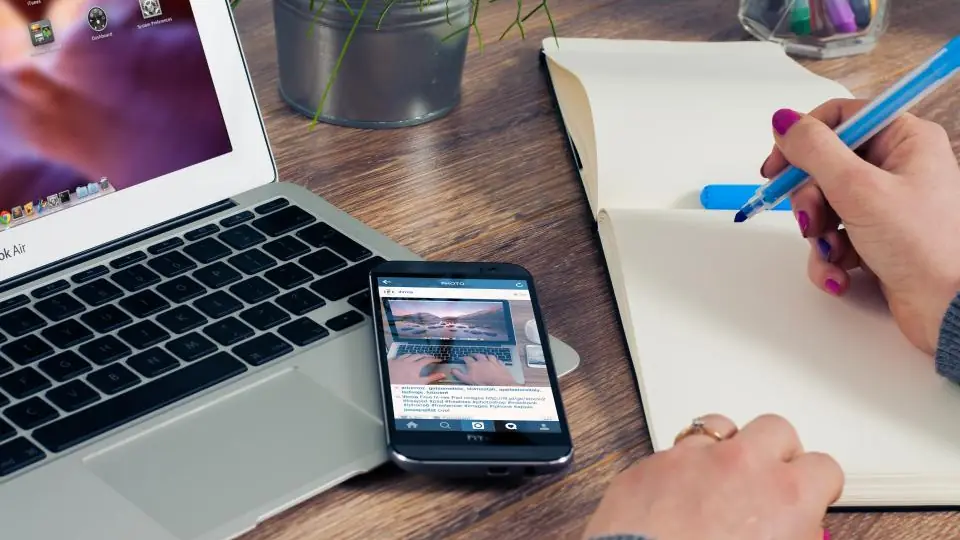 A person writing notes beside a laptop and phone while drafting a follow-up email