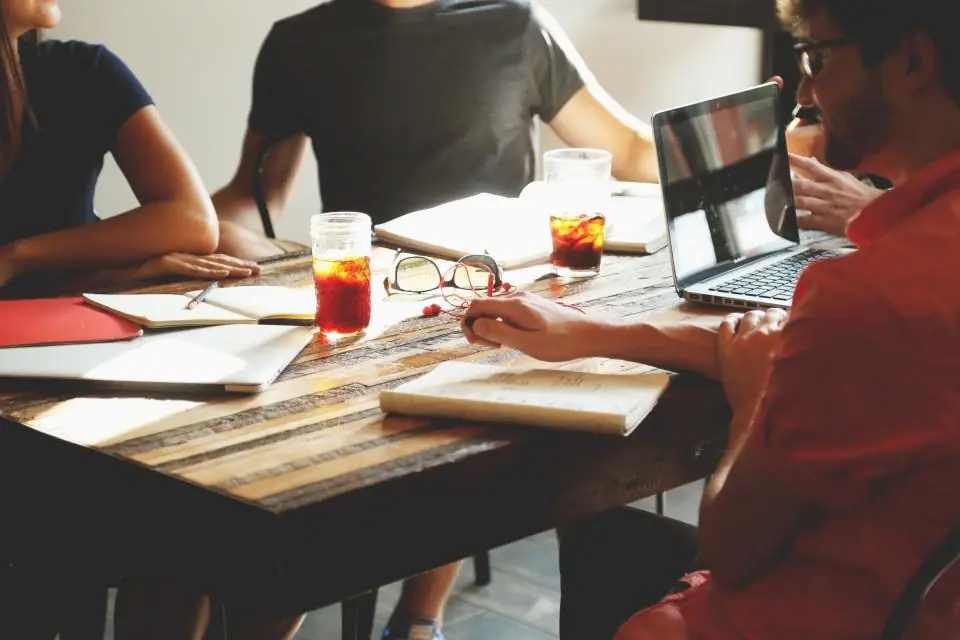 A small team meeting around a wooden table with laptops and notebooks