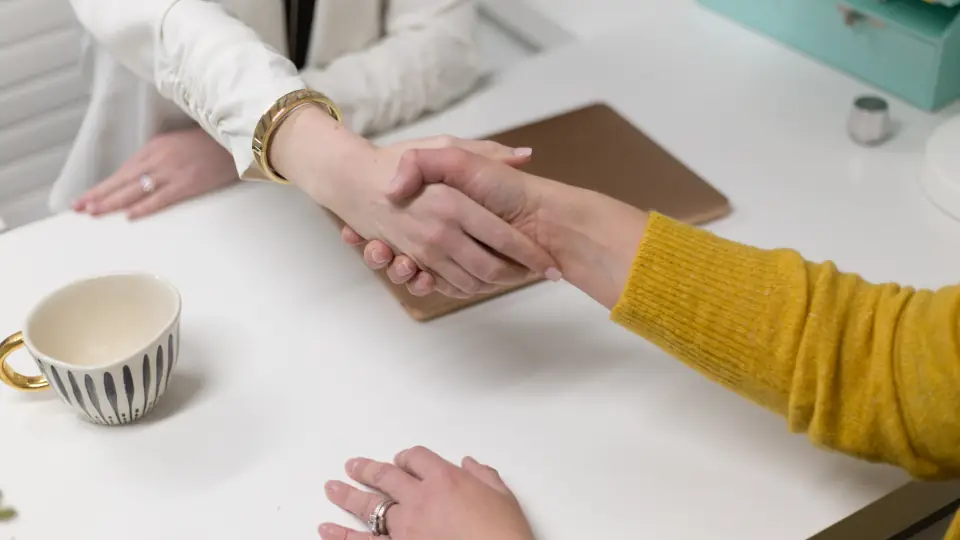 Two people shaking hands across a white desk after agreeing a job offer