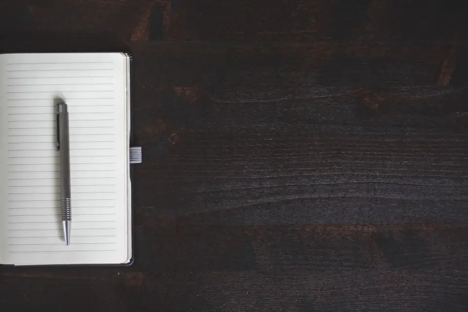 A closed notebook and pen on a dark wooden table