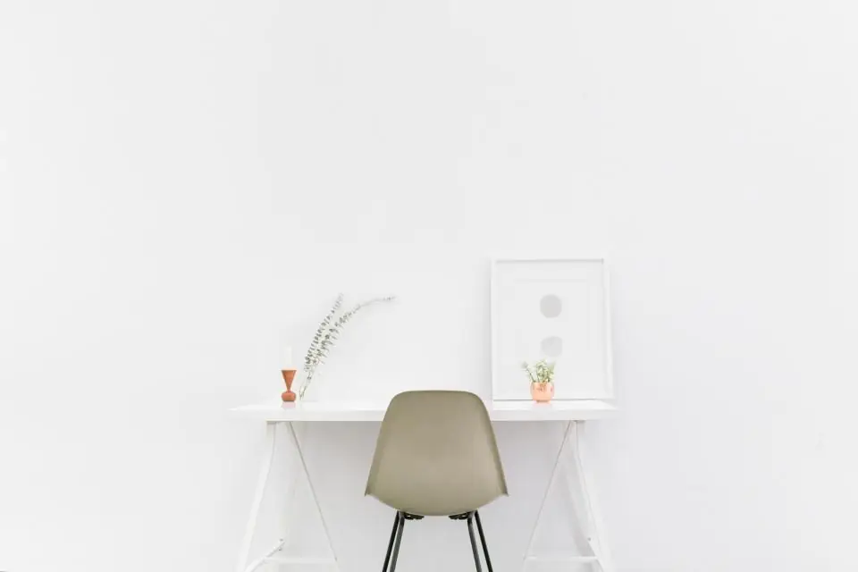 A bright, empty desk and chair by a white wall after an employee has left