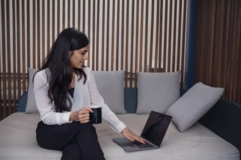 Woman sitting on a sofa with a laptop and a mug, waiting to hear back about a job application