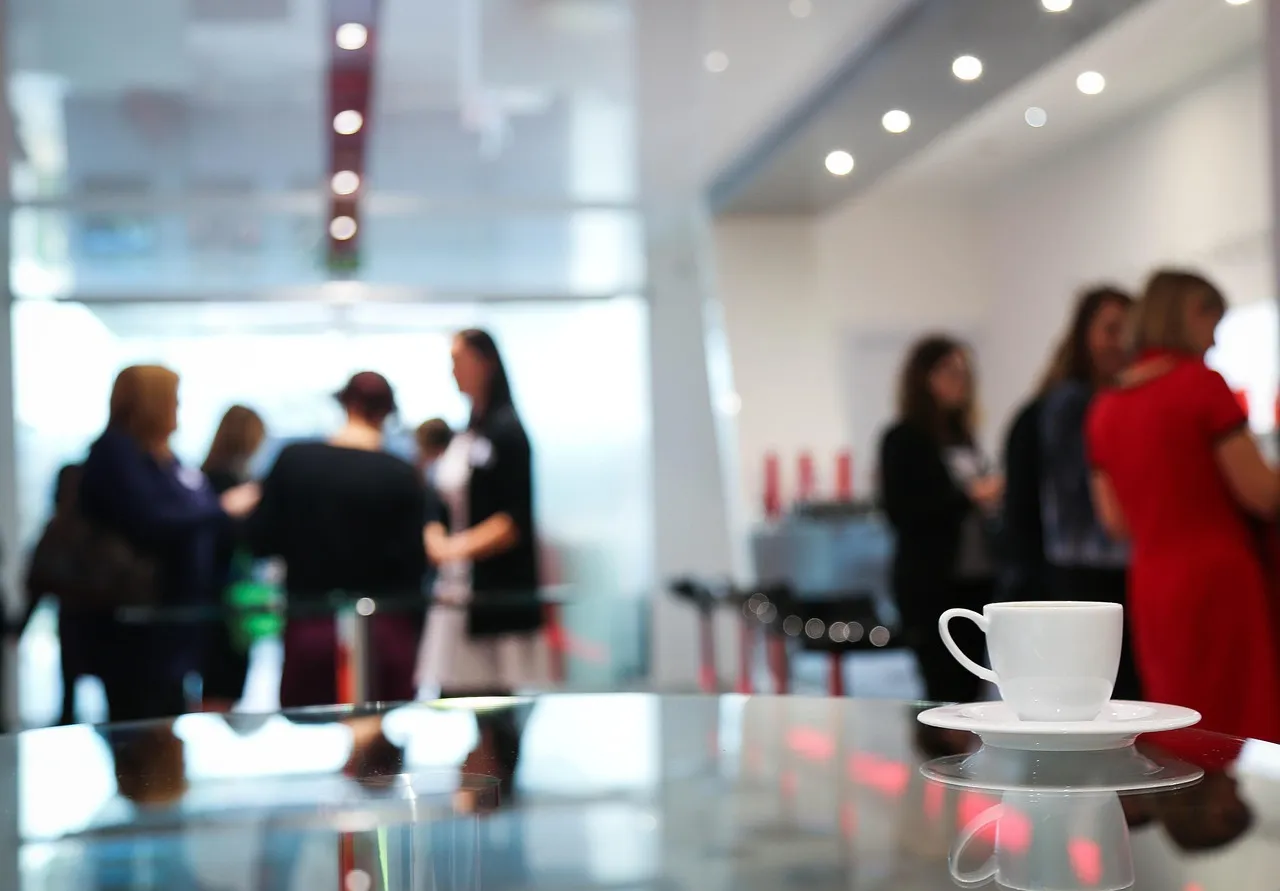 Blurred group of professionals talking in a bright lobby behind a white coffee cup