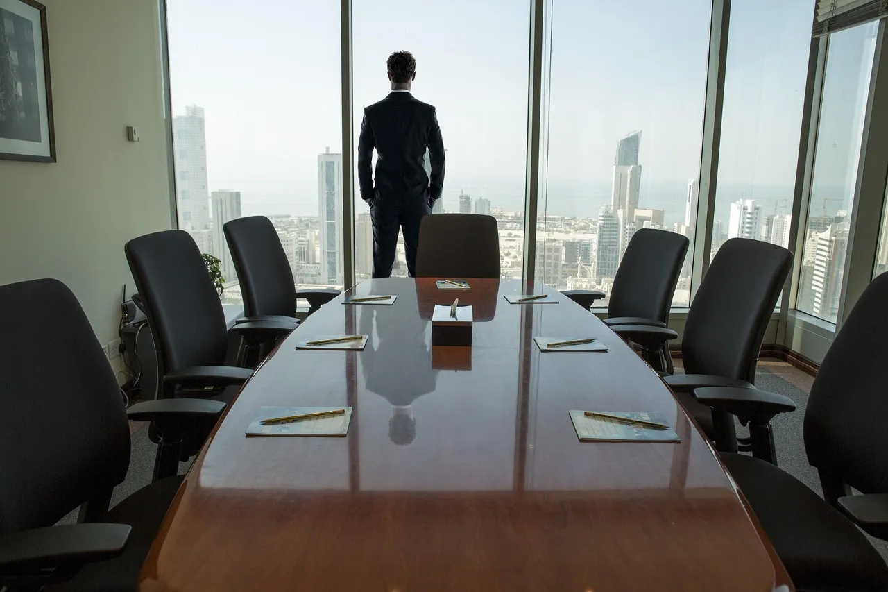 Businessman standing at the window of an empty boardroom overlooking a city
