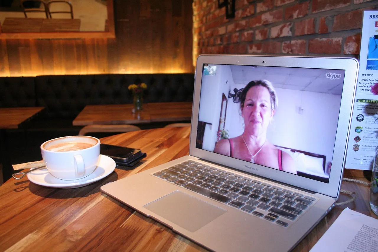 Laptop on a cafe table showing a video call, next to a cup of coffee