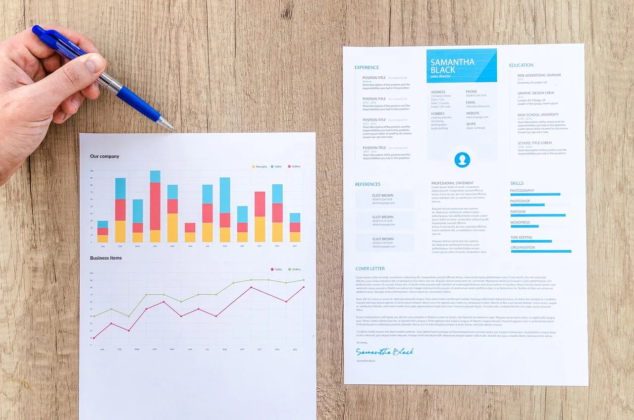 Printed one-page resume beside a chart, with a hand holding a pen over the desk