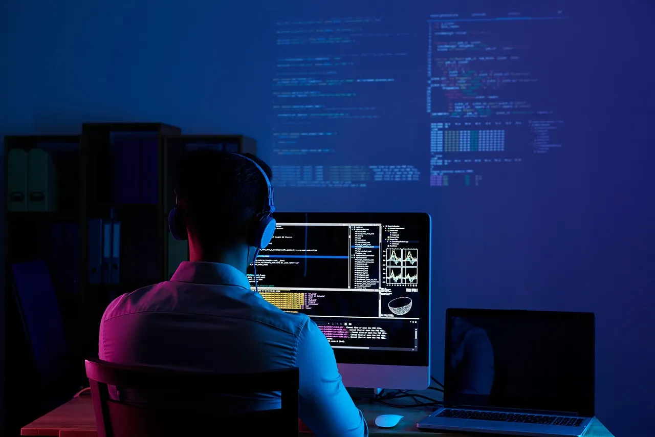 Developer in headphones working at a monitor of code in a dark room with code projected on the wall