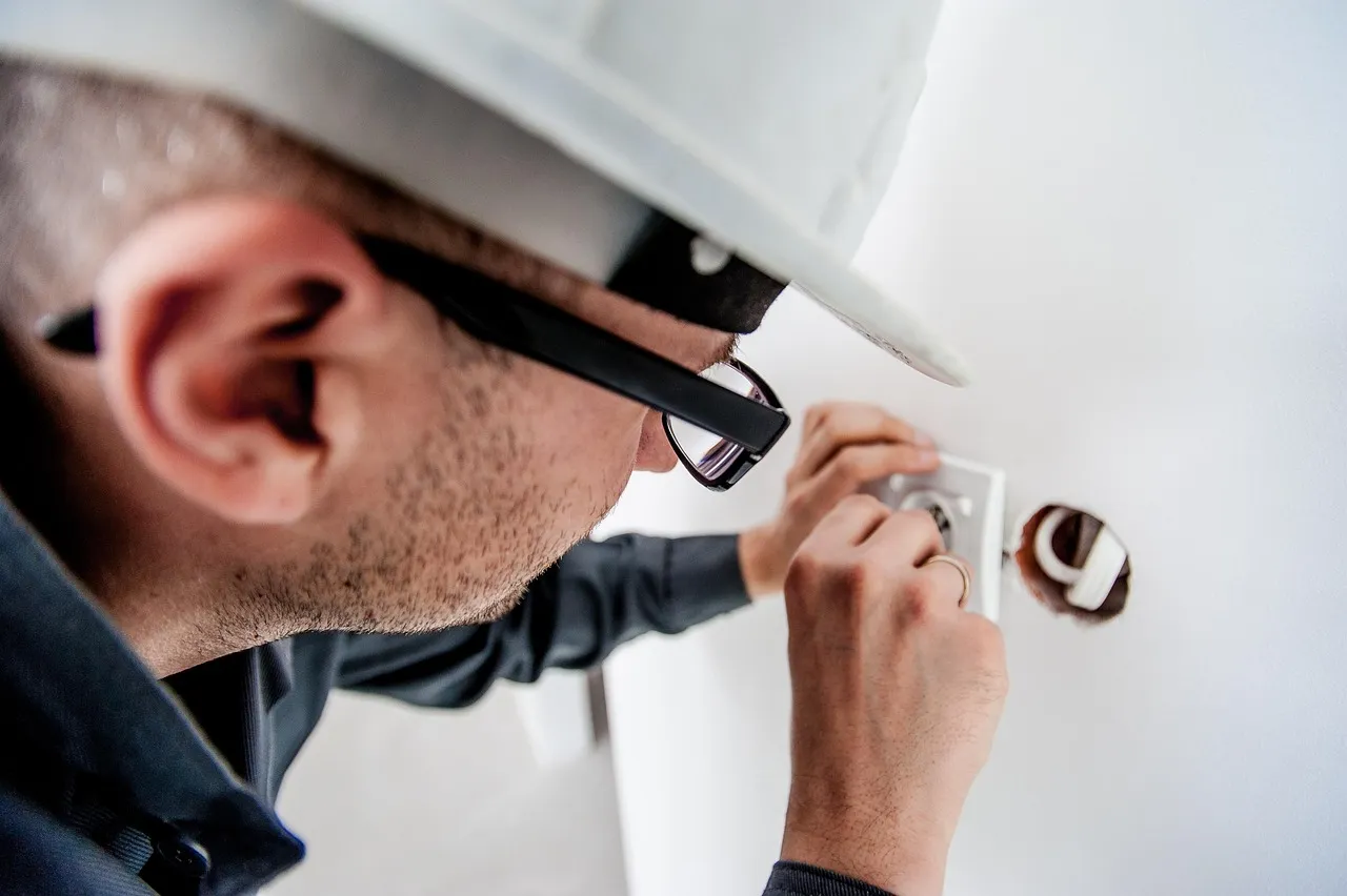Electrician in a white hard hat and glasses fitting a wall socket