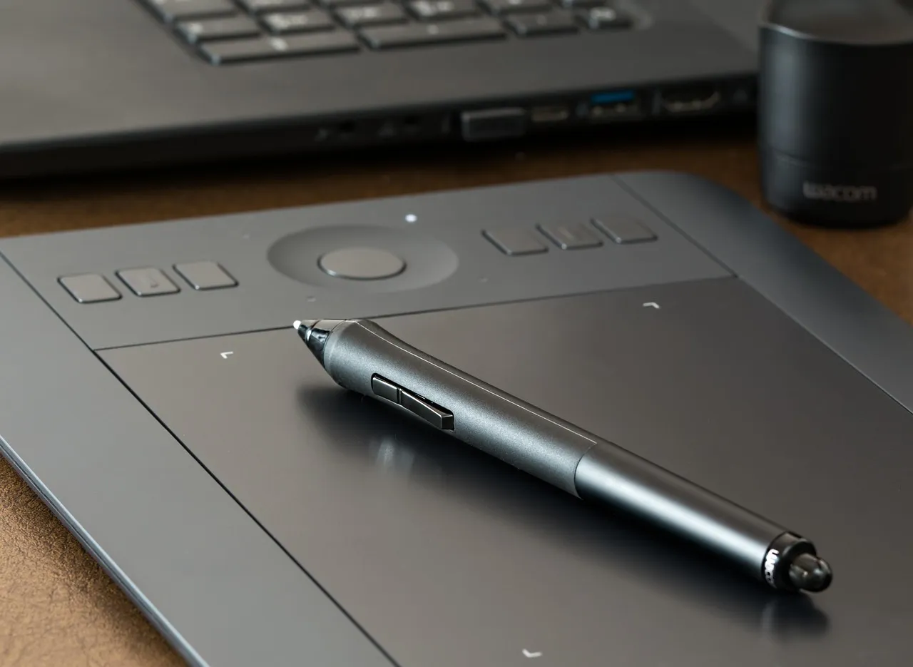 Graphics drawing tablet and stylus pen in front of a laptop keyboard