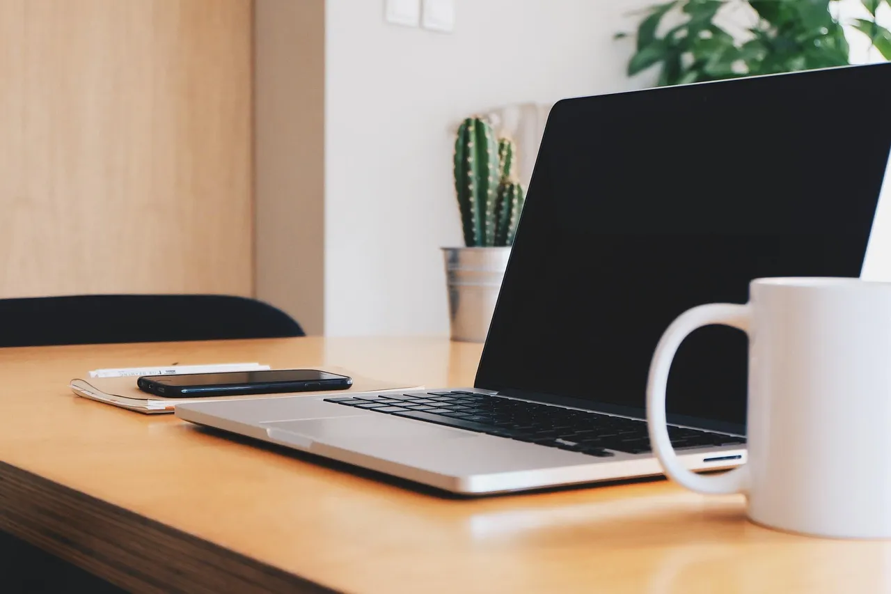 Laptop and white mug on a wooden desk in a home office with plants