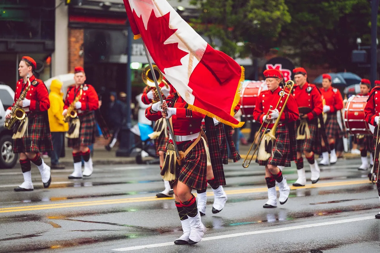 Marching band in red tartan uniforms carrying a Canadian flag down a wet street