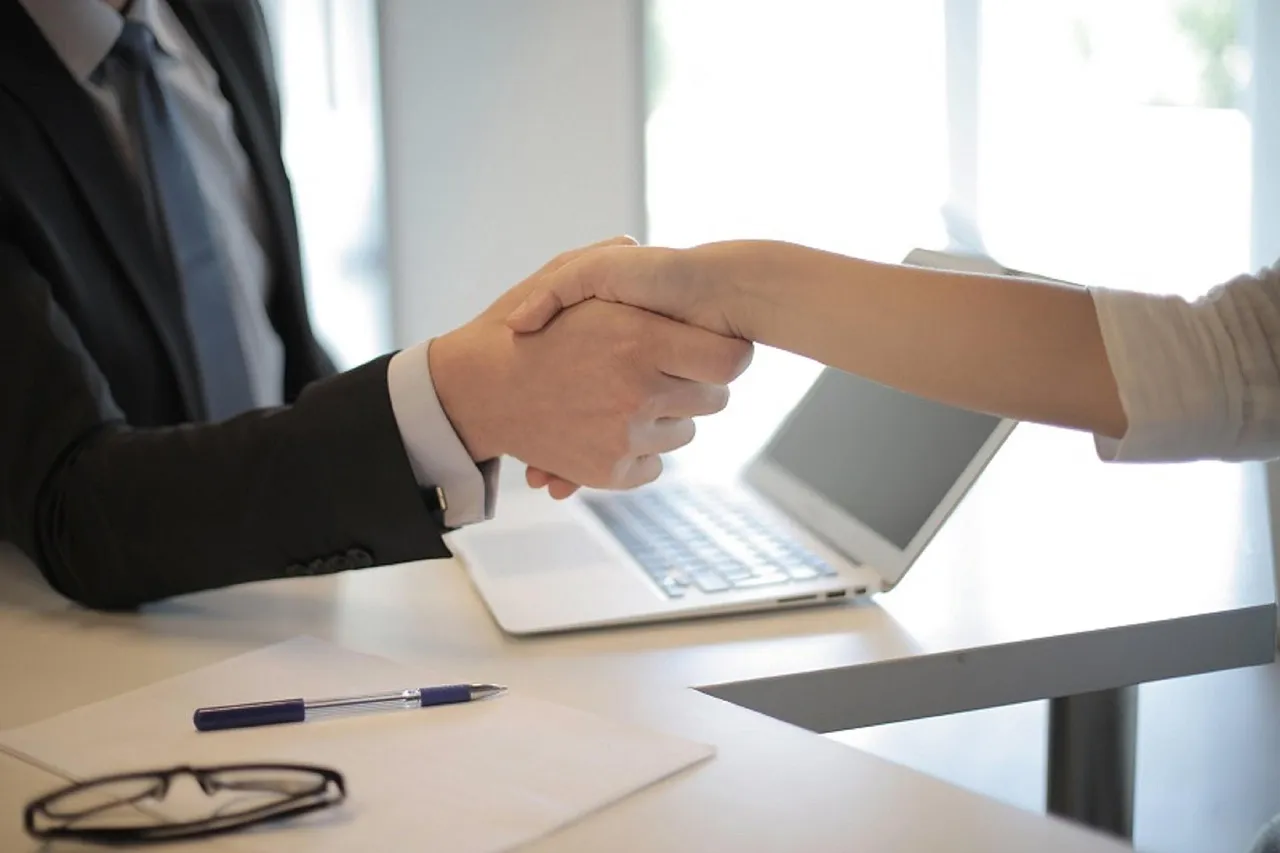 Two people shaking hands across a table at a job interview