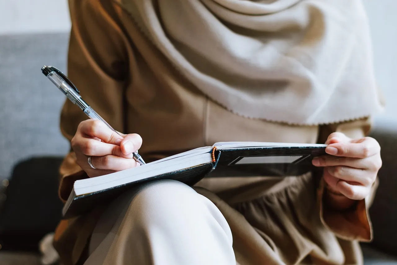 Woman in a headscarf writing in a notebook on her lap