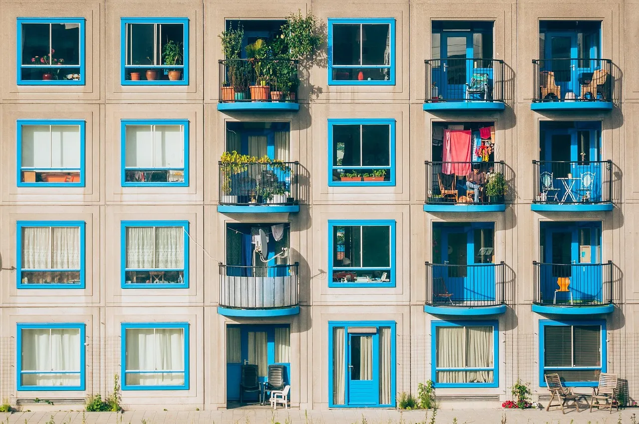 Apartment block facade with blue-framed windows and balconies full of plants and laundry