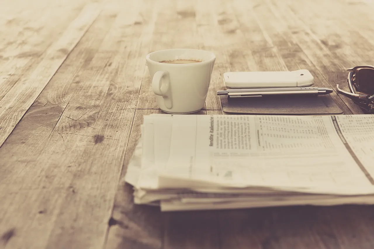 Folded newspapers beside a cup of coffee on a wooden table