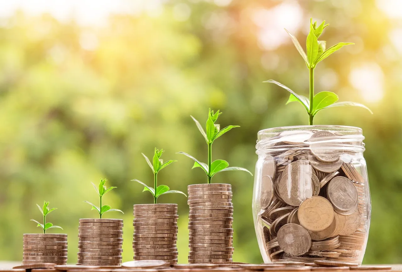 Rising stacks of coins with seedlings growing from them beside a glass jar of coins