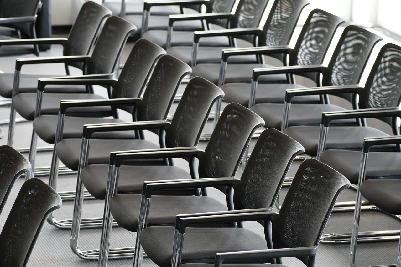 Rows of empty black chairs in a meeting hall