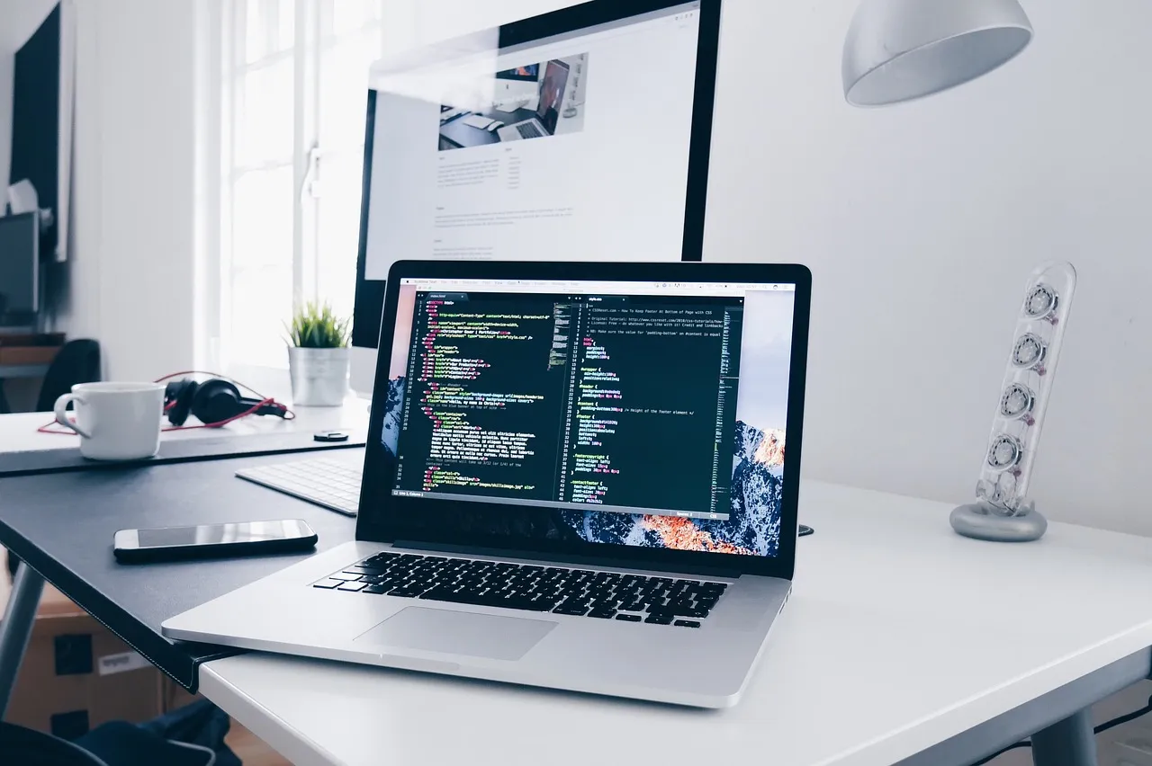 Laptop showing code on a white desk next to a desktop monitor
