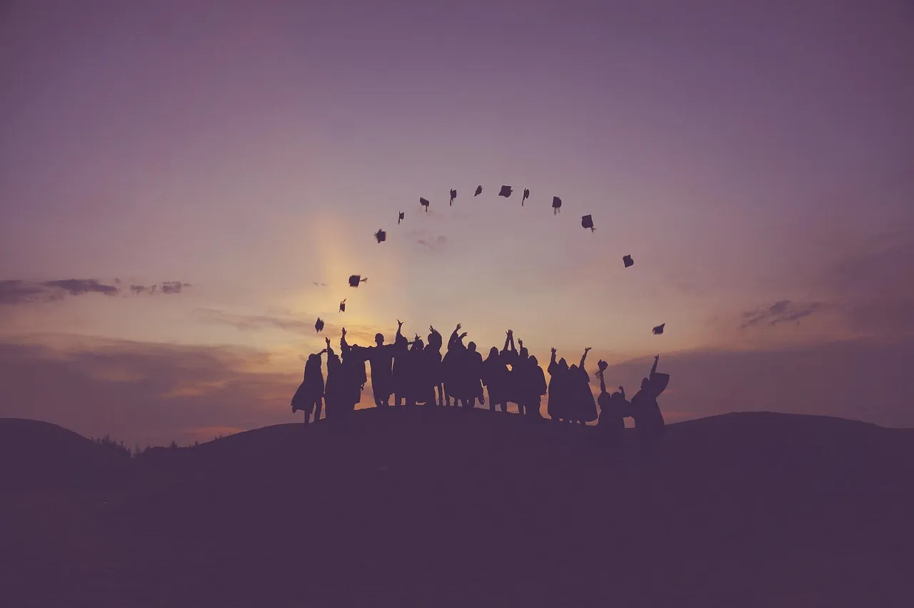 Silhouetted graduates on a hilltop tossing their caps into a purple sunset sky