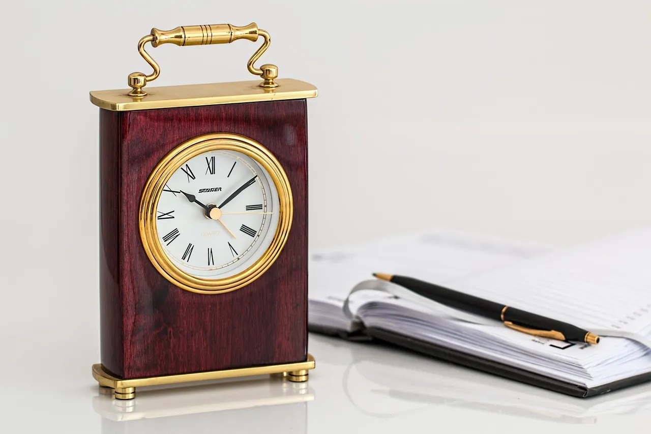 Wooden desk clock beside an open notebook and pen