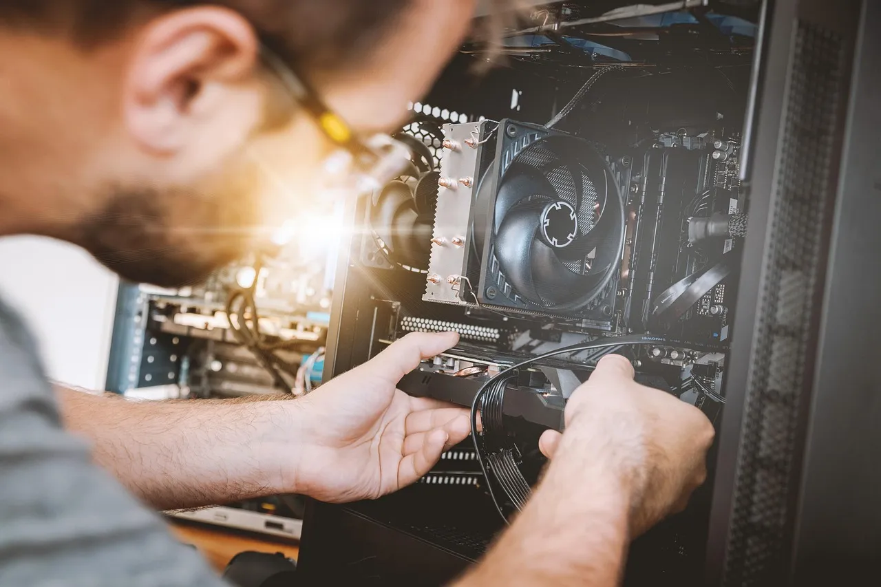 Technician in glasses connecting a cable inside an open desktop PC beside the CPU cooler