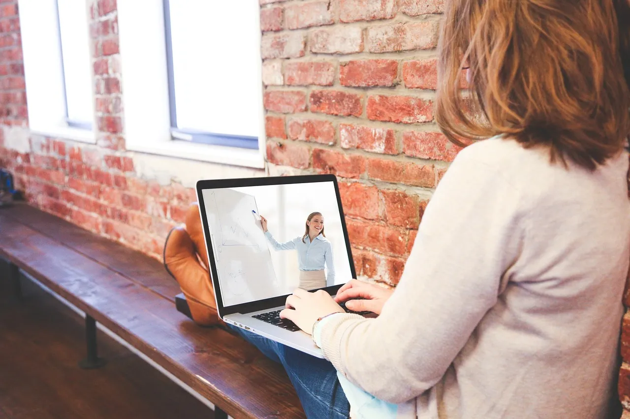 Woman on a video call on her laptop beside a brick wall