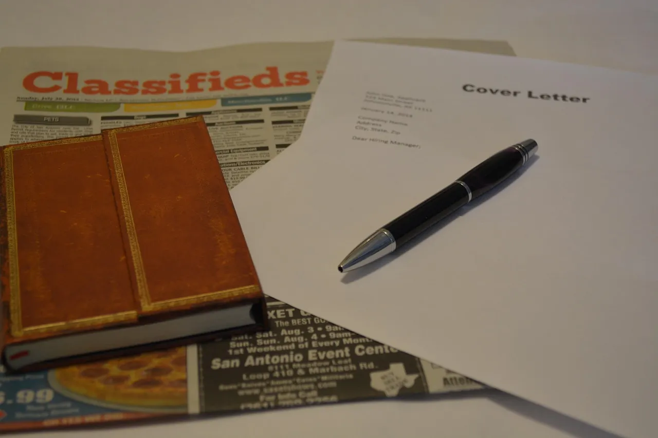Cover letter and pen on top of newspaper classified job ads and a notebook