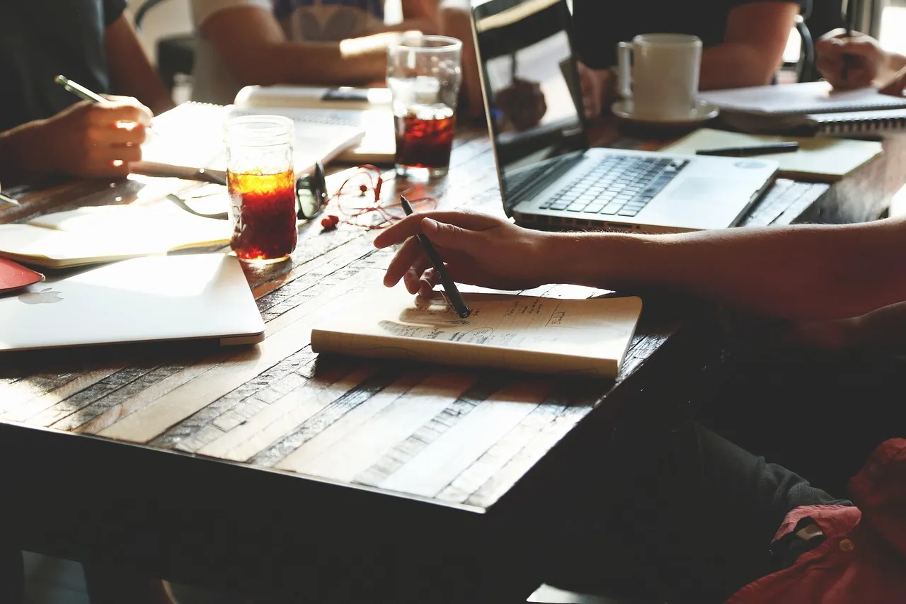 People working at a wooden table with notebooks, laptops and coffee